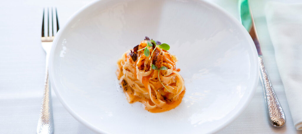 Immagine in primo piano di un piatto di tagliatelle affumicate con ricci di mare e limone