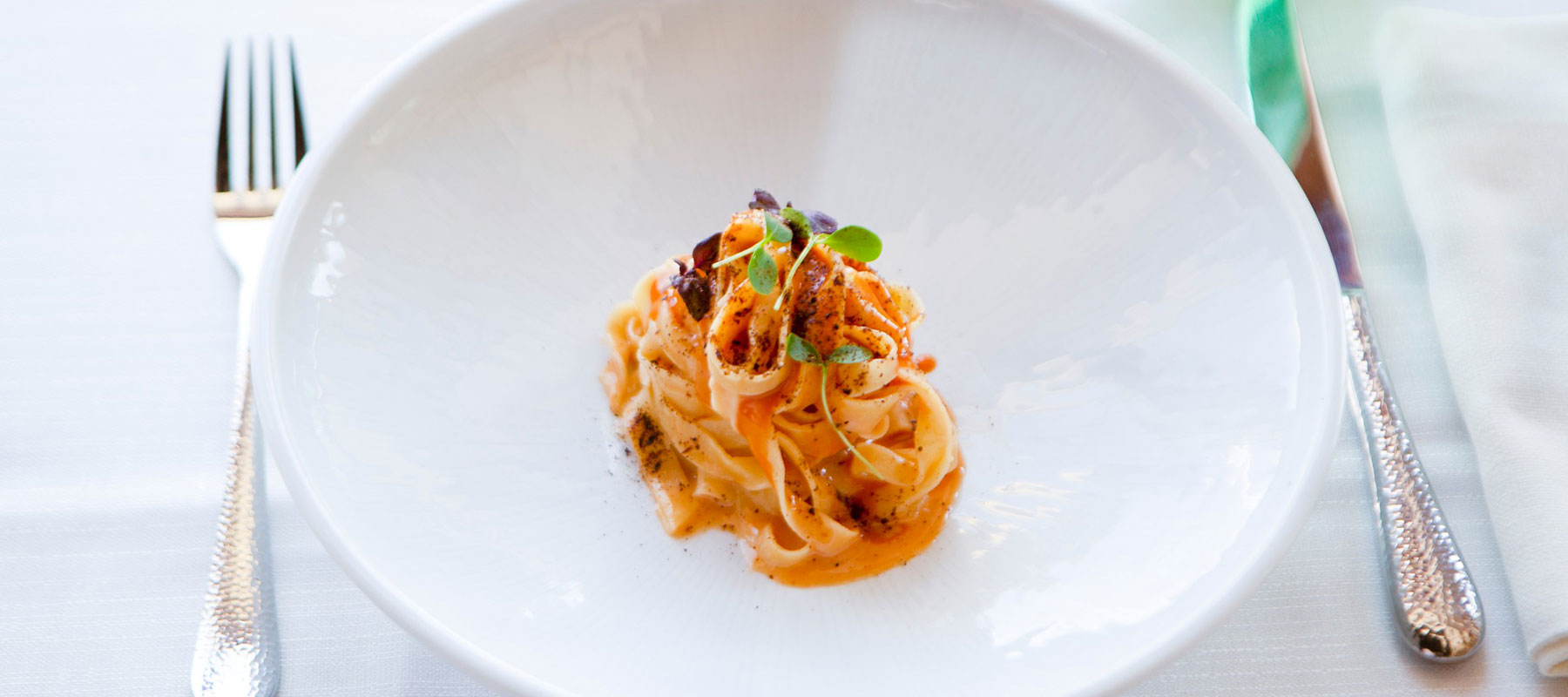 Immagine in primo piano di un piatto di tagliatelle affumicate con ricci di mare e limone
