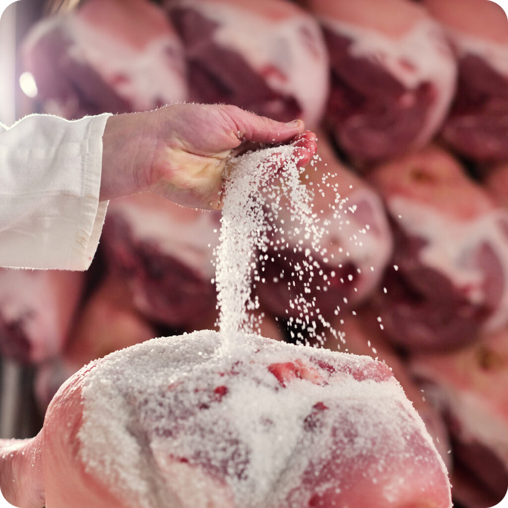 Una mano colma di sale che viene rovesciato su un prosciutto.